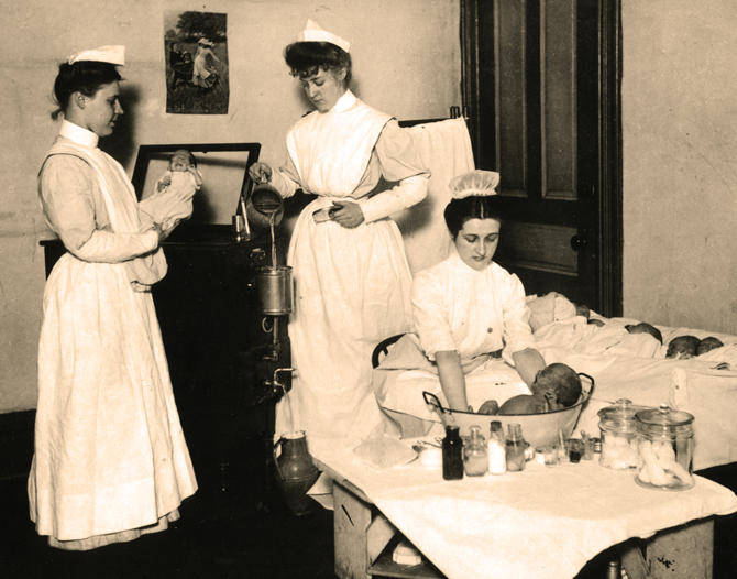 Three nurses at work in the Presbyterian Hospital infant nursery, c1910. Illinois Training School for Nurses graduate washes baby while two Presbyterian Hospital School of Nursing students filter water for incubator. From the Subject Photograph Collection